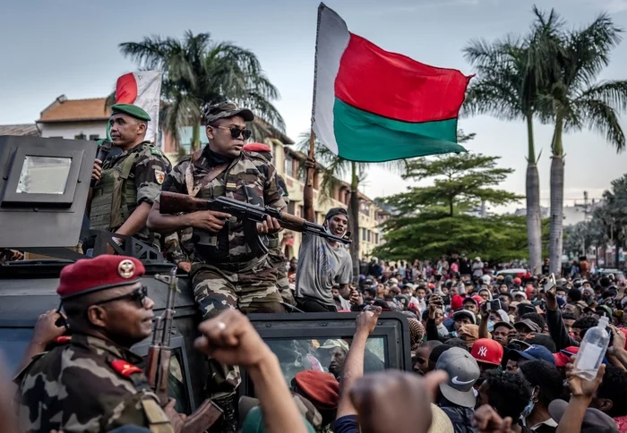 Madagascar Gen Z protesters wave national flags under army watch in October 2025.