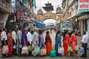 Nepal NRs 100 Customs Crackdown: People standing in long queue with bags at India–Nepal border checkpoint as trucks pass through decorated market street amid strict NRs 100 customs enforcement