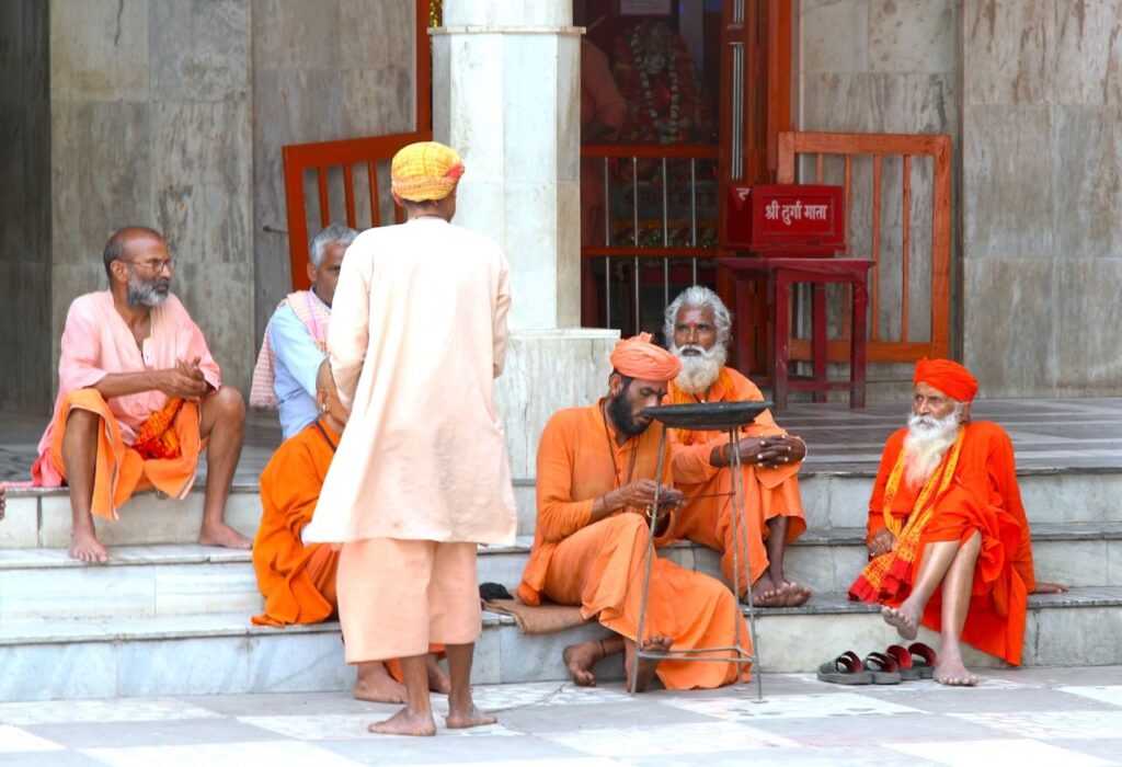 A group of sadhus/yogis sitting and relaxing on the steps of the Ma Durga Temple at Gorakhnath Temple, engaged in conversation.