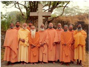 Saffron-Robed Christian Monks walking with wooden sticks and a large cross in background during Good Friday procession in Kerala