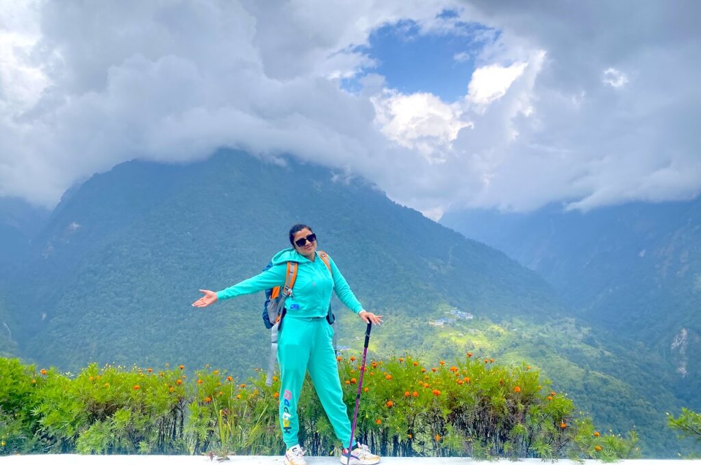 Trekker standing with a hiking pole on a mountain viewpoint above a lush green valley in the Annapurna region, surrounded by dramatic cloud-covered peaks on the first day of the trek.