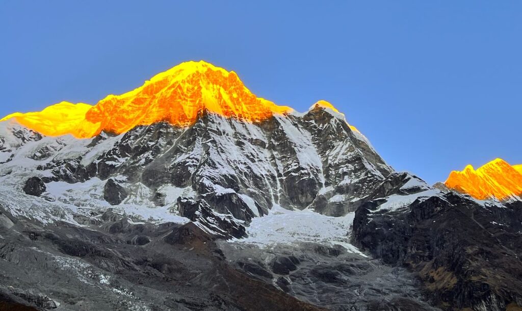 Annapurna Base Camp sunrise view with golden sunlight illuminating the snow-covered Annapurna massif in the Nepal Himalayas.