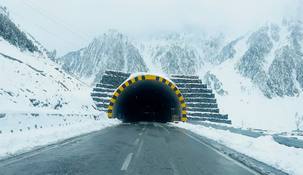 Road leading into a tunnel portal surrounded by heavy snow and steep Himalayan slopes.